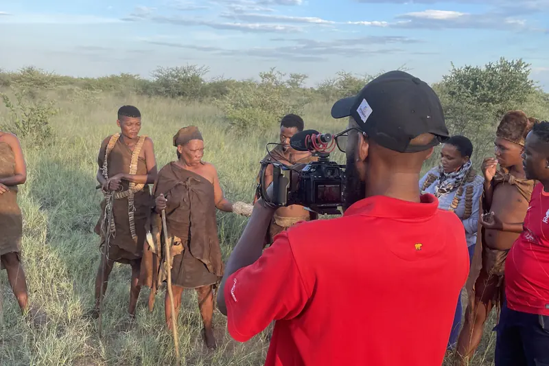 Shatho Tibone filming a group of San community members in open Kalahari grassland at golden hour